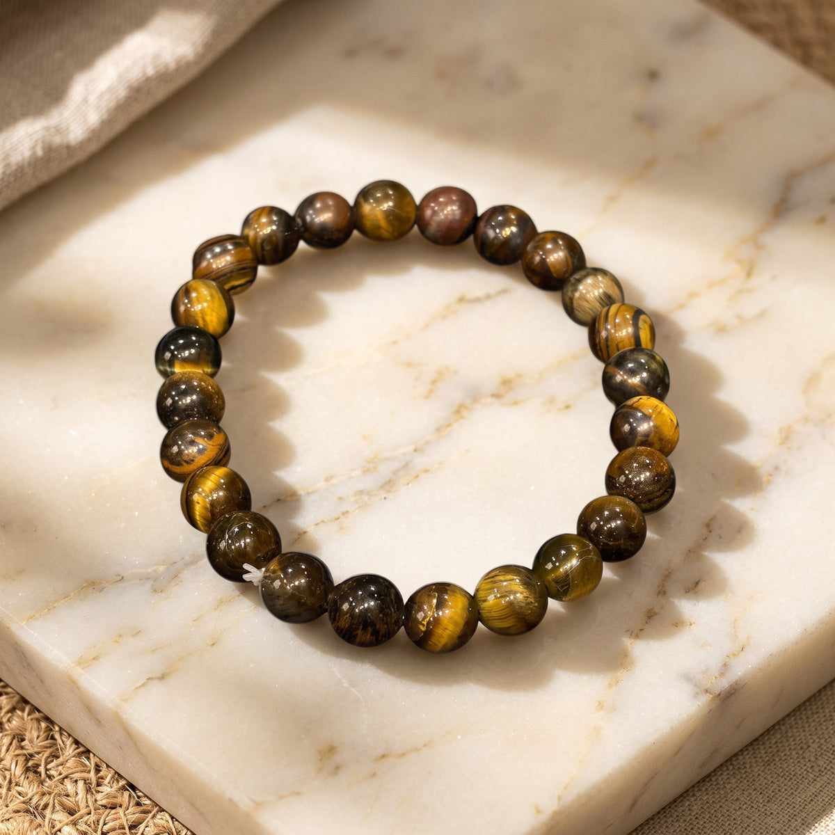 Shri Divya Ratan natural Tiger Eye crystal bead bracelet with golden-brown chatoyant shimmer on a marble surface.