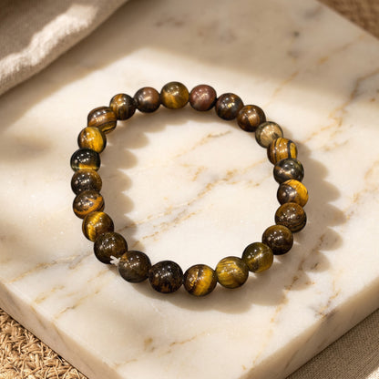Shri Divya Ratan natural Tiger Eye crystal bead bracelet with golden-brown chatoyant shimmer on a marble surface.